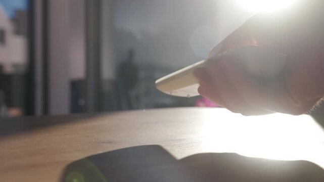 Hand taking air conditioner remote control lying on table in morning sunlight. Concept of cooling temperature control and hot weather comfort