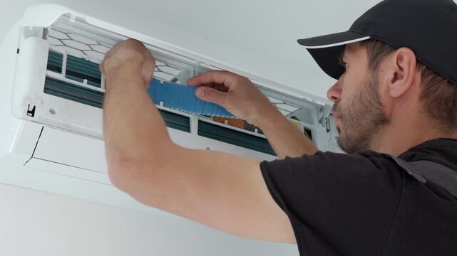 Technician chtcking air conditioner filter inside an open wall unit. Concept of HVAC maintenance cleaner airflow and cooling system care.