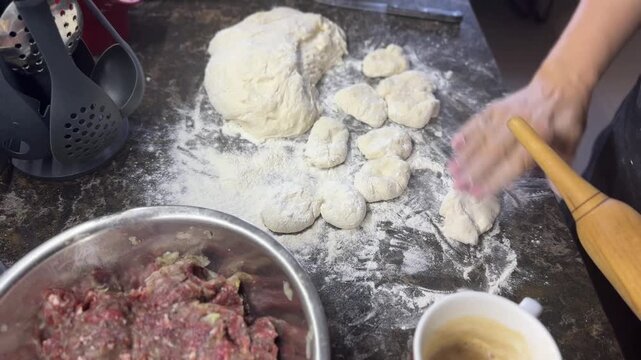 Women's hands dust with flour and roll out dough balls for pies. Top view..