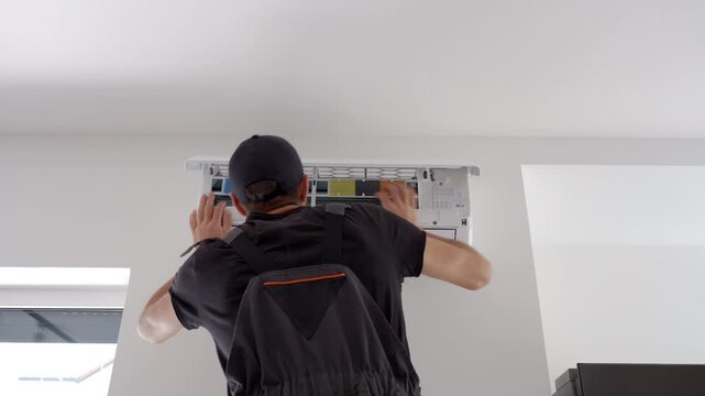 Back view of man opens a wall air conditioner to check and clean the filter. Concept of AC cleaning air conditioner repair and home cooling service.