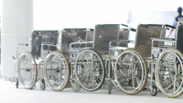 Row of hospital wheelchairs parked outside medical facility entrance with security guard in healthcare service