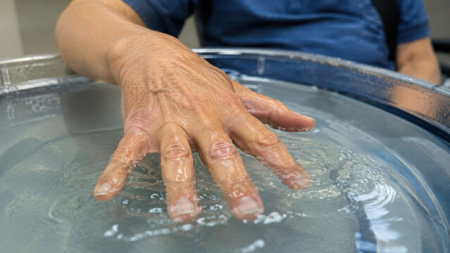 Hand performing finger extension exercise in water therapy basin for rehabilitation treatment with physical therapist assistance during occupational recovery session