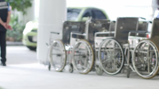 Row of hospital wheelchairs parked outside medical facility entrance with security guard in healthcare service