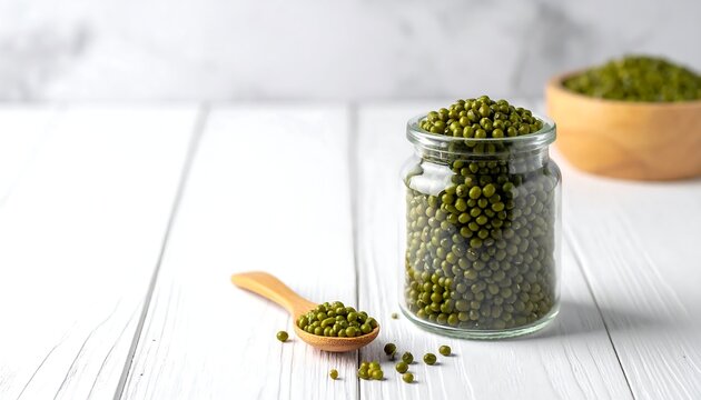 Green mung beans filling a glass jar with wooden spoon and bowl on white wooden boards, gray wall background