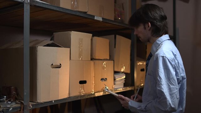 Man reviewing inventory in a storage room with cardboard boxes
