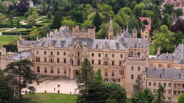 Aerial drone view of Lednice Castle front facade with the surrounding town and open agricultural countryside visible beyond, Moravia, Czech Republic.