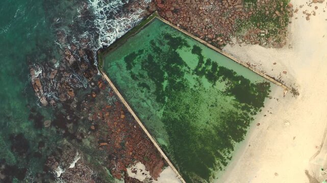 Aerial view of a green algae bloom in a coastal enclosure near the beach and ocean waves.
