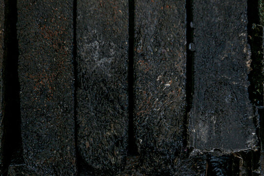 Recycled plastic waste is compressed into ecobricks. This photo shows an arrangement of rectangular, black-brown ecobricks with a rough, textured surface resembling melted plastic fibers.