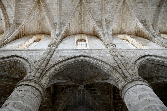 Low-angle view looking up at the medieval Gothic stone arches, ribbed vaulted ceiling, and upper clerestory windows of the historic Bugday Camii in Famagusta.