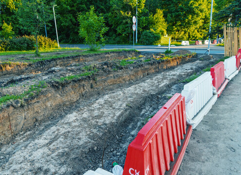 Road excavation beside green trees with plastic safety barriers