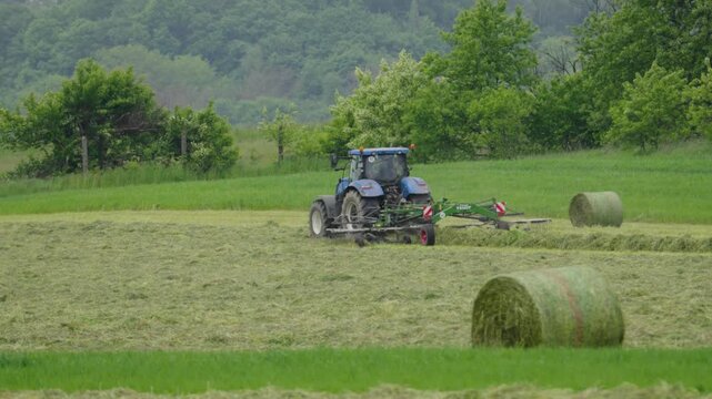 Modern tractor bales grass into round hay bales during forage harvesting in a field