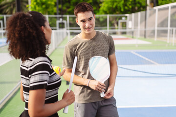 Naklejka premium Pickleball sports player team talking on outdoor court. Smiling man and woman holding paddle and yellow ball discussing match.