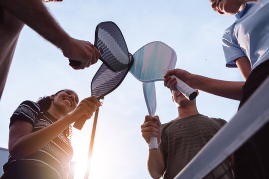 Diverse group of friends hitting their pickleball paddles together. Teamwork, friendship, and active lifestyle concept at an outdoor sports court.