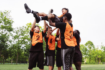 Fototapeta premium Diverse soccer team lifting a teammate to celebrate victory on the field. Teamwork, success, and champion concept during an amateur football match.