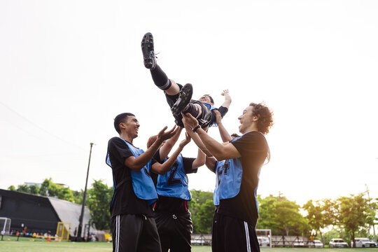Soccer team tossing teammate in the air to celebrate victory. Low angle view, teamwork, success, and active lifestyle concept.