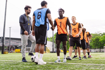 Soccer players shaking hands with a coach watching on the field. Sportsmanship, respect, and professional sports concept. © Kiattisak