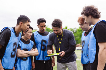 Coach explaining tactics and strategy to soccer players on the field. Teamwork, planning, and professional leadership concept in sports. © Kiattisak
