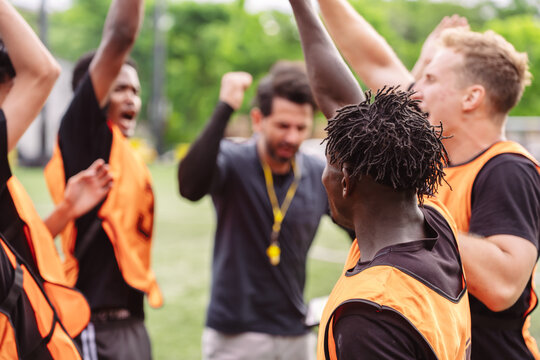 Soccer team and coach raising hands together to motivate before a match. Teamwork, unity, and spirit concept on the field.