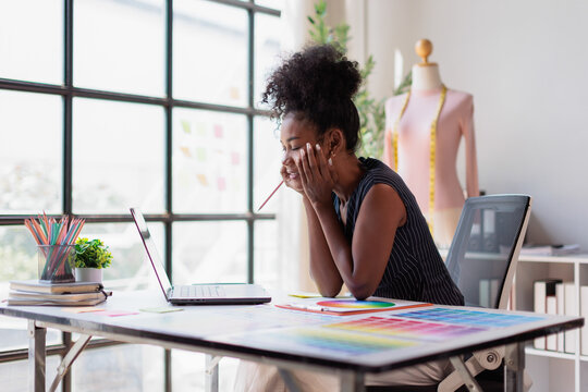 Black woman fashion designer concentrating on work, looking at laptop while brainstorming ideas for new clothing line in creative studio office