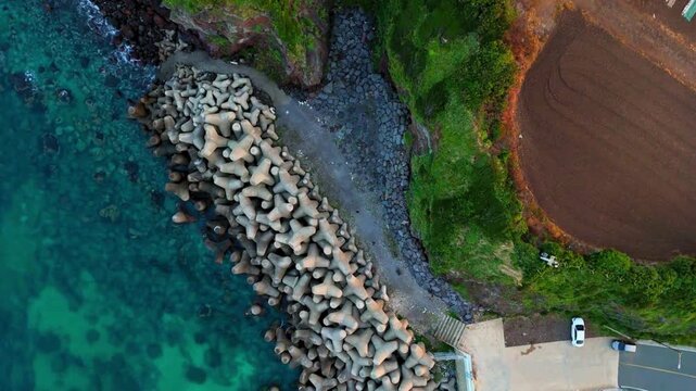 Top-down aerial view of tetrapod breakwater pier and coastal cliff, Jeju Island, South Korea
