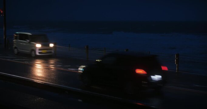 Evening shot of traffic on wet, Japanese road near crashing waves of sea