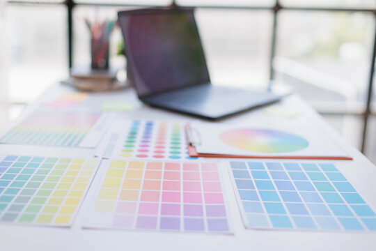 Designer workspace displaying color swatches, palettes, and a color wheel chart on a table with a laptop in the background, representing creativity and design process