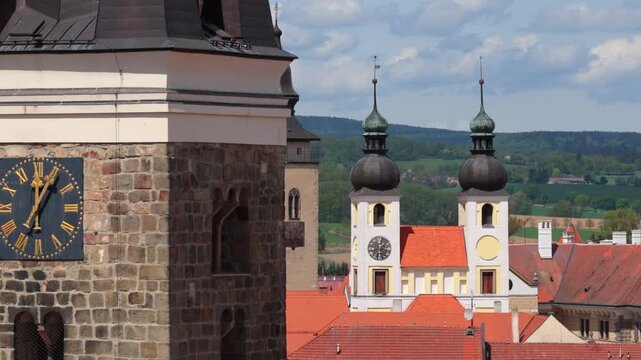 Aerial drone view of a historic Czech town with a Gothic clock tower, colorful Renaissance main square, castle complex, and surrounding ponds amid spring countryside, Telc, Czech Republic