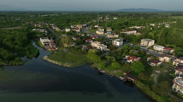 High angle drone shot of Anaklia village surrounded by lush green forests, agricultural fields, and a winding river under bright daylight.