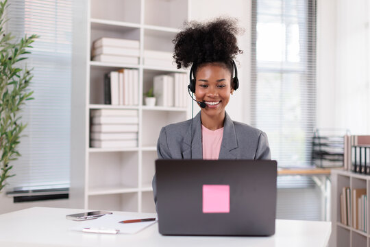African american woman working at her desk, wearing a headset with a microphone, providing online support and actively engaging in a virtual meeting or call while smiling