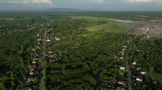 High angle drone shot of Anaklia village surrounded by lush green forests, agricultural fields, and a winding river under bright daylight.