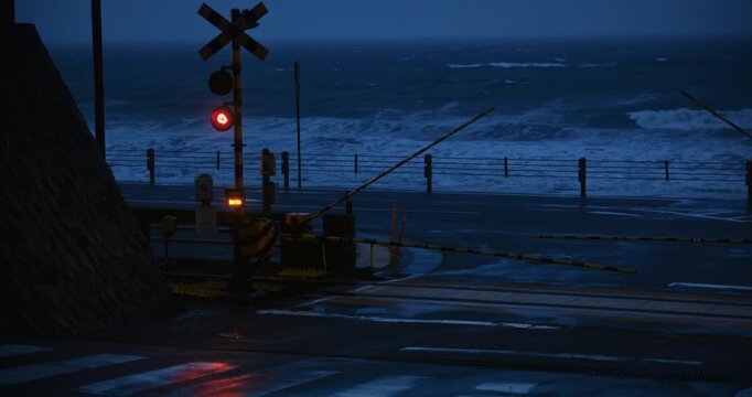 Crossing Sign and Lowered Gate Foreground With Rough Sea In Coastal Japan At Night