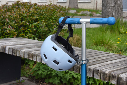 Child's blue helmet hanging on a scooter handle at a park bench, safe