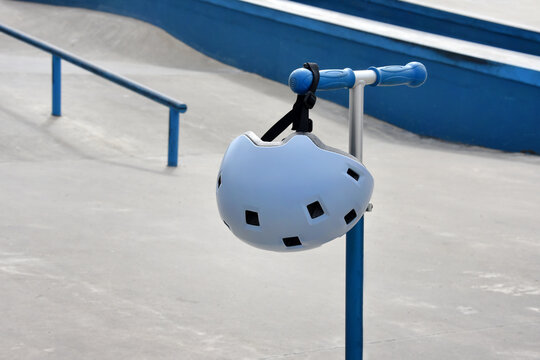 Child scooter with helmet hanging on handlebar at a blue skatepark
