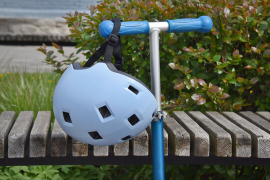 Child's blue helmet hanging on a scooter handle at a park bench, safe