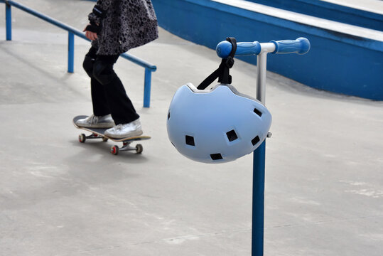 Child scooter with helmet hanging on handlebar at a blue skatepark