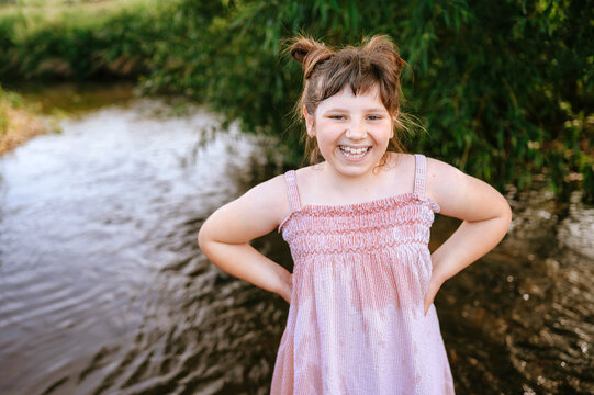 Smiling young girl standing beside a shallow stream in summer