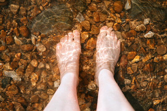 Bare feet standing in clear shallow stream over pebbles