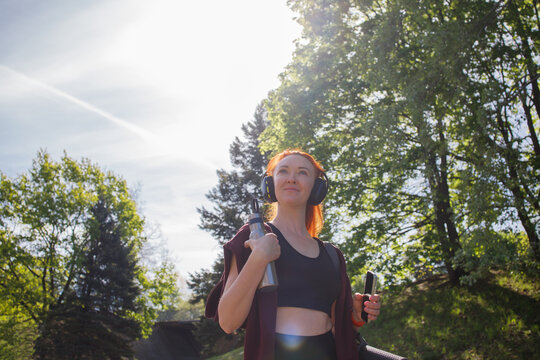 Redhaired middleaged sporty woman with yoga mat, headphones and smart