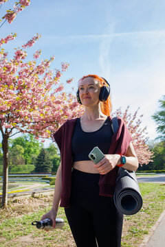 Redhaired middleaged sporty woman with yoga mat, headphones and smart