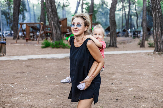 Happy woman gives a toddler a piggyback ride outdoors