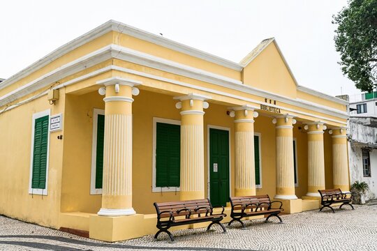 Beautiful yellow facade of historic colonial Coloane Library building built in 1911 with white columns and green wooden shutters in Macau China