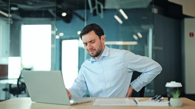 Close up of corporate manager or IT specialist suffering from backache, kidney pain or spinal tension at laptop. Tired employee or freelance designer feeling sharp lumbar spasm during office work
