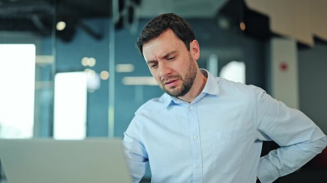 Close up of overworked corporate employee or IT specialist feeling lower back tension, posture problem or lumbar cramp at laptop. Stressed manager or freelance worker suffering from spine fatigue