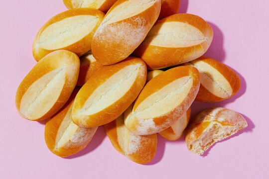 Pile of fresh bolillo bread rolls with scored crust on a pink surface for traditional bakery marketing, culinary blogging and artisanal food styling