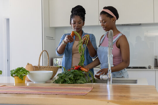 African American mom and teen daughter prepping at kitchen island cutting carrots rinsing tomatoes