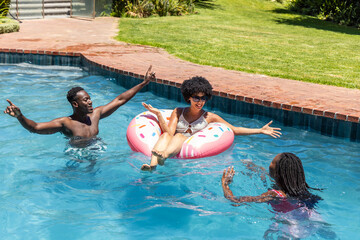 Obraz premium African American friends playing in backyard pool on sunny day with pink donut float