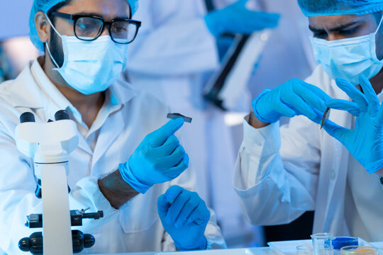Two scientists wearing masks and gloves examine small components in a modern research laboratory with a microscope.
