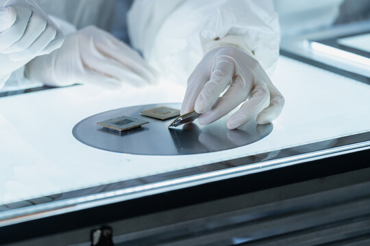 Close-up of a technician's gloved hands carefully inspecting semiconductor microchips and a silicon wafer on an illuminated light table in a cleanroom laboratory.