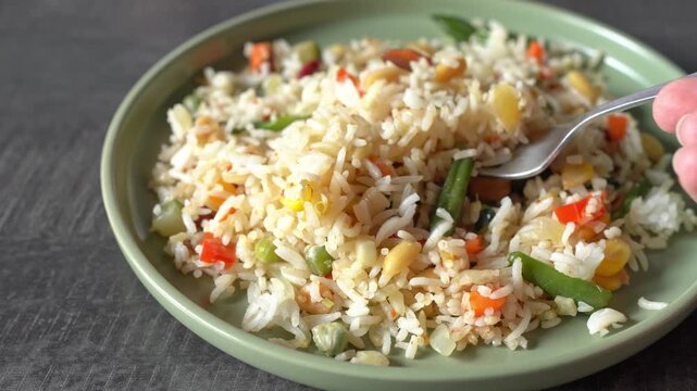 An unidentified woman is mixing rice and vegetables in a plate. The concept is a lack of appetite. 