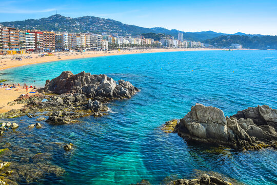 Scenic view of Lloret de Mar beach, coastal town and sea with prominent rocks in the foreground, Spain.